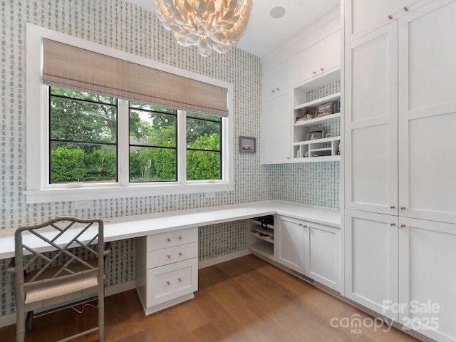 unfurnished office featuring built in study area, light wood-type flooring, wallpapered walls, and a notable chandelier