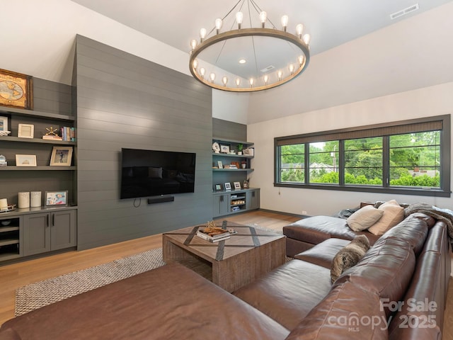 living area featuring visible vents, baseboards, light wood-type flooring, a chandelier, and built in shelves