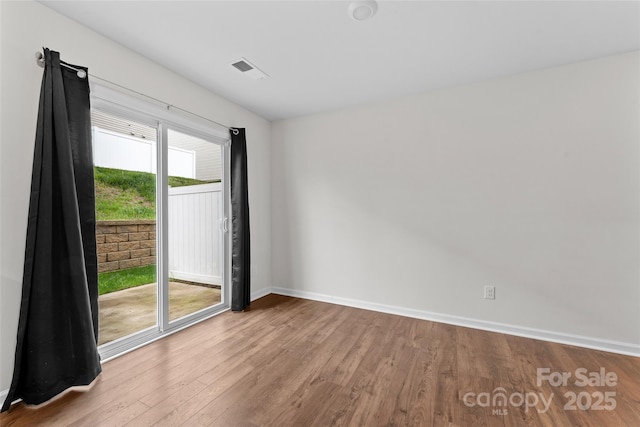 empty room featuring wood finished floors, visible vents, and baseboards