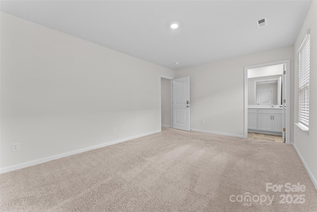 unfurnished bedroom featuring visible vents, ensuite bathroom, baseboards, and light colored carpet