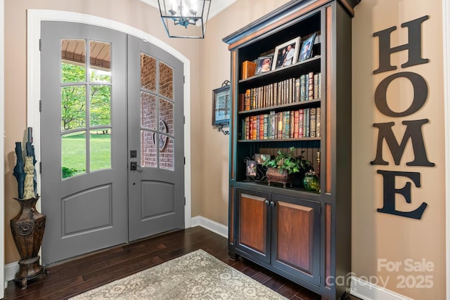 foyer entrance with a notable chandelier, baseboards, and dark wood-style flooring