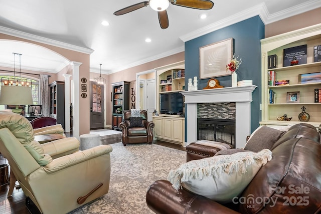 living room featuring ceiling fan with notable chandelier, a glass covered fireplace, ornate columns, ornamental molding, and recessed lighting