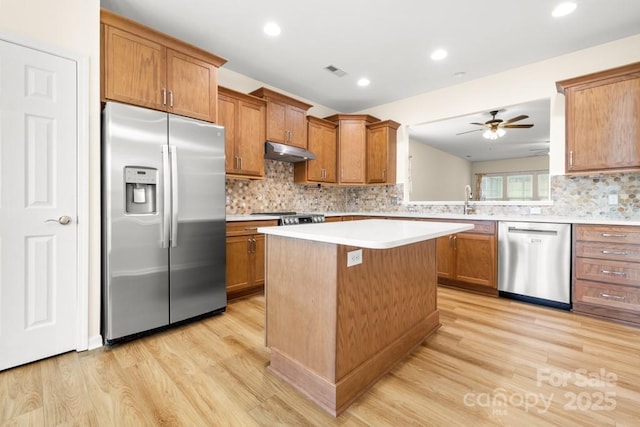 20135 Dovekie Ln, Fort Mill, SC 29707 - kitchen with brown cabinets, stainless steel appliances, a kitchen island, under cabinet range hood, and light wood-type flooring