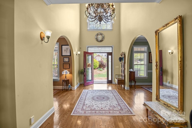foyer with arched walkways, wood finished floors, a notable chandelier, and a wealth of natural light
