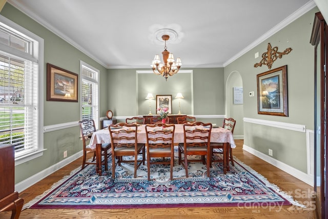 dining area with baseboards, arched walkways, ornamental molding, a chandelier, and dark wood-type flooring