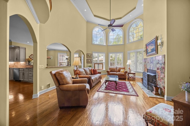 living area with baseboards, ornamental molding, a tiled fireplace, ceiling fan, and wood-type flooring