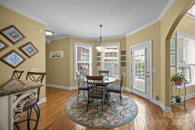dining room with arched walkways, baseboards, ornamental molding, and wood finished floors