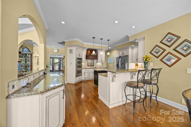 kitchen featuring ornamental molding, light stone counters, a peninsula, dark wood-style floors, and stainless steel appliances