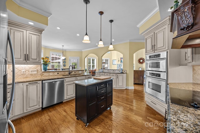 kitchen featuring arched walkways, a sink, appliances with stainless steel finishes, a peninsula, and light wood-style flooring