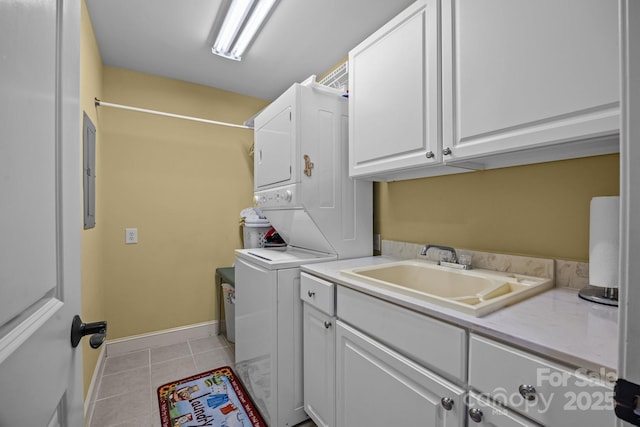 laundry room featuring light tile patterned floors, stacked washer and dryer, a sink, baseboards, and cabinet space