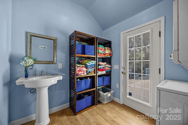entryway with baseboards, vaulted ceiling, washer / dryer, visible vents, and light wood finished floors