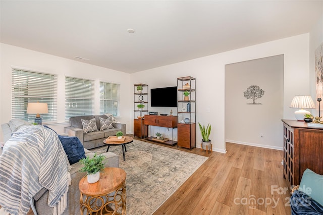 living area featuring light wood-style floors, baseboards, visible vents, and a wealth of natural light