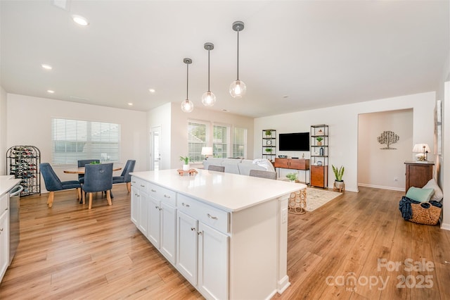 kitchen with light countertops, white cabinets, a kitchen island, and light wood-style flooring