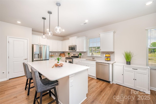 kitchen featuring a kitchen bar, appliances with stainless steel finishes, a sink, white cabinets, and light wood-style flooring