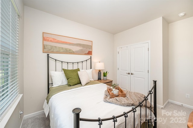 bedroom with baseboards, a closet, and light colored carpet