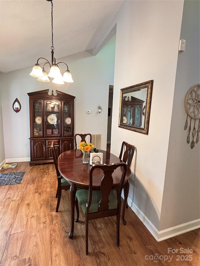dining area with light wood-type flooring, baseboards, and an inviting chandelier