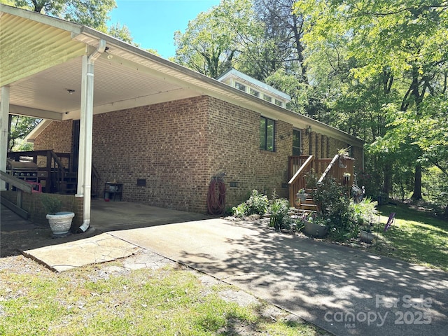 view of side of home featuring stairs, driveway, brick siding, and an attached carport