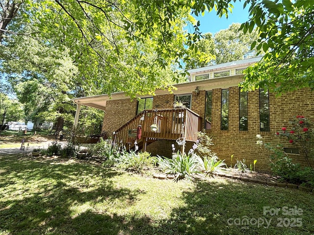 exterior space with a lawn, a wooden deck, and brick siding