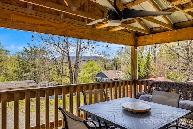 wooden deck with a mountain view, outdoor dining space, and ceiling fan