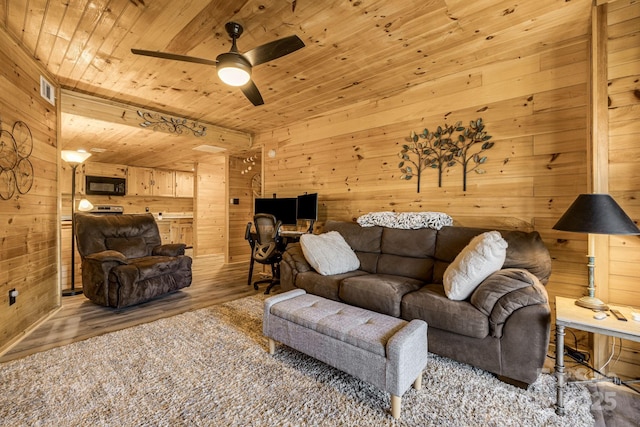 living area featuring light wood finished floors, wooden ceiling, wood walls, and a ceiling fan