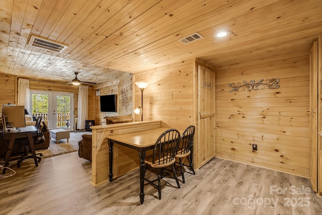dining space featuring light wood-style flooring, wooden ceiling, wooden walls, and visible vents