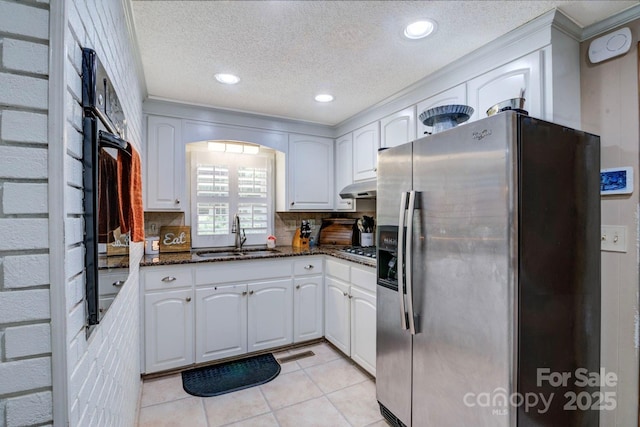 kitchen with dark stone counters, a textured ceiling, a sink, stainless steel appliances, and under cabinet range hood