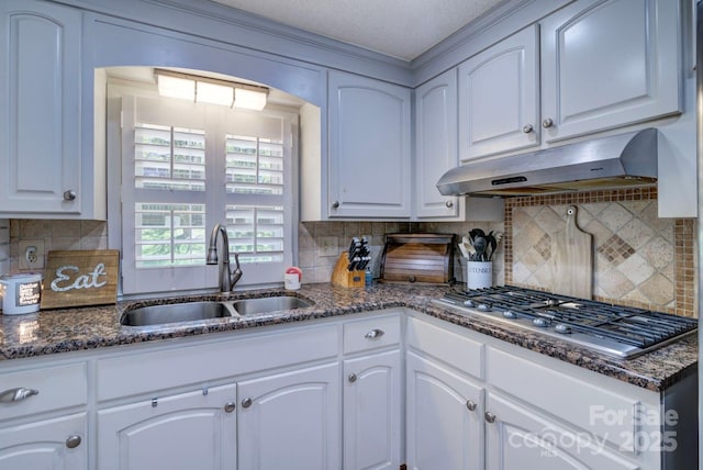 kitchen with stainless steel gas cooktop, under cabinet range hood, a sink, and dark stone countertops