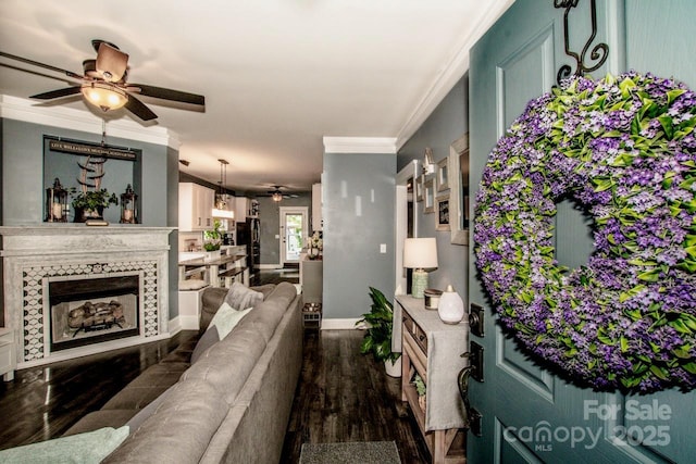 living area featuring dark wood-style flooring, baseboards, ornamental molding, ceiling fan, and a premium fireplace