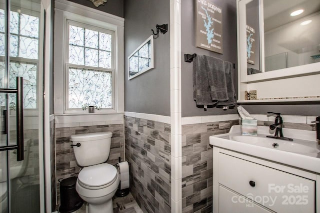 bathroom with toilet, tile walls, a wainscoted wall, and a healthy amount of sunlight