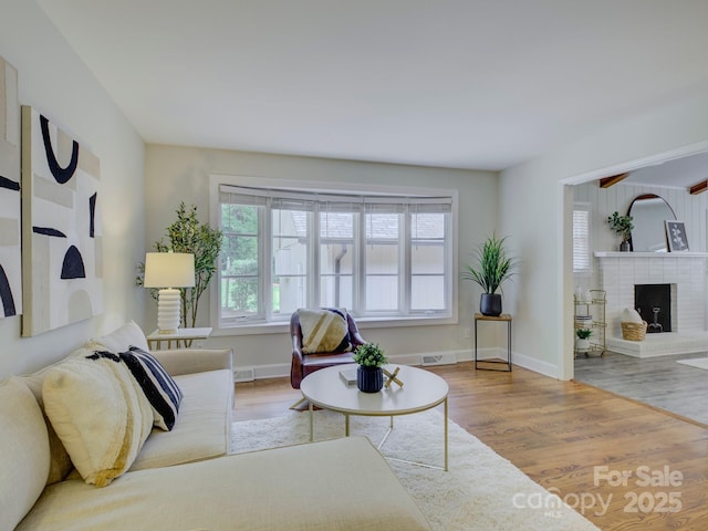 living area with a fireplace, wood finished floors, visible vents, and baseboards