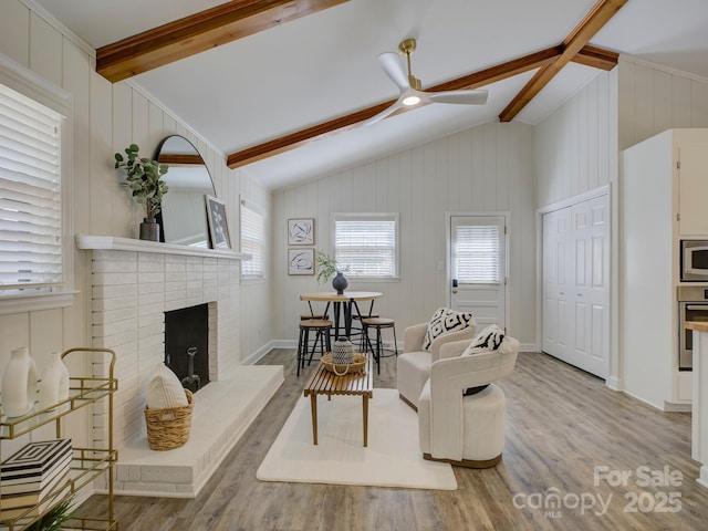living room with wood finished floors, vaulted ceiling with beams, baseboards, a fireplace, and ceiling fan