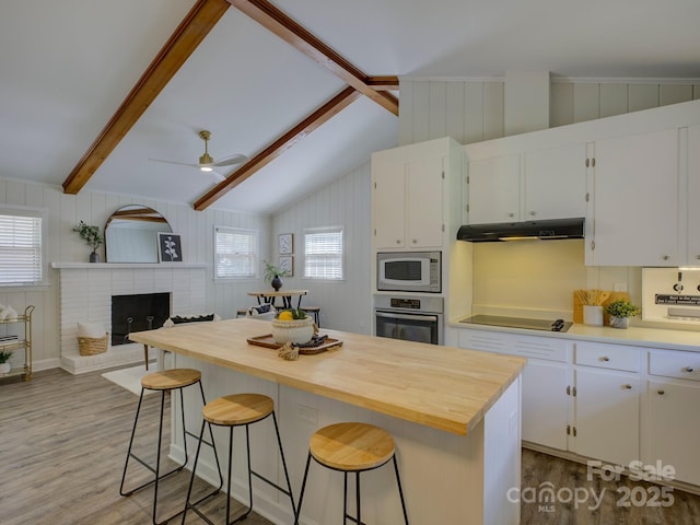 kitchen with under cabinet range hood, wood finished floors, a healthy amount of sunlight, white microwave, and stainless steel oven