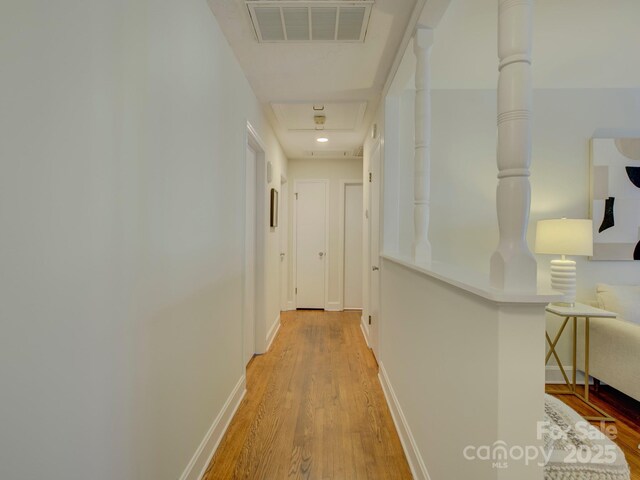 hallway featuring attic access, light wood-style floors, visible vents, and baseboards