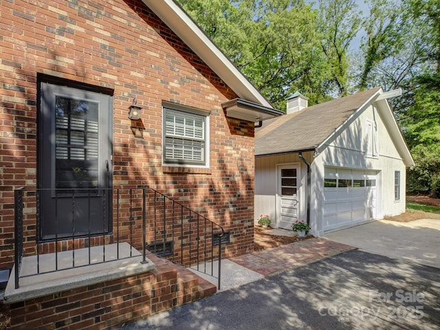 exterior space featuring driveway, an outbuilding, brick siding, and a chimney