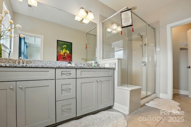 bathroom featuring a sink, double vanity, a stall shower, baseboards, and tile patterned flooring