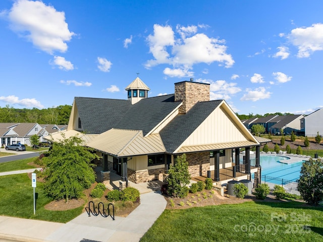 view of front of house with roof with shingles, a community pool, a front yard, a standing seam roof, and metal roof