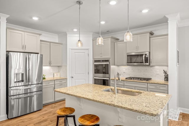 kitchen featuring decorative columns, a sink, light wood-style floors, a breakfast bar, and stainless steel appliances