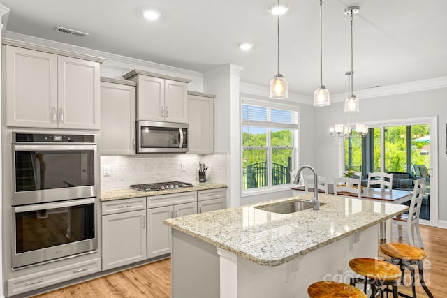kitchen with appliances with stainless steel finishes, ornamental molding, a sink, and light wood-type flooring