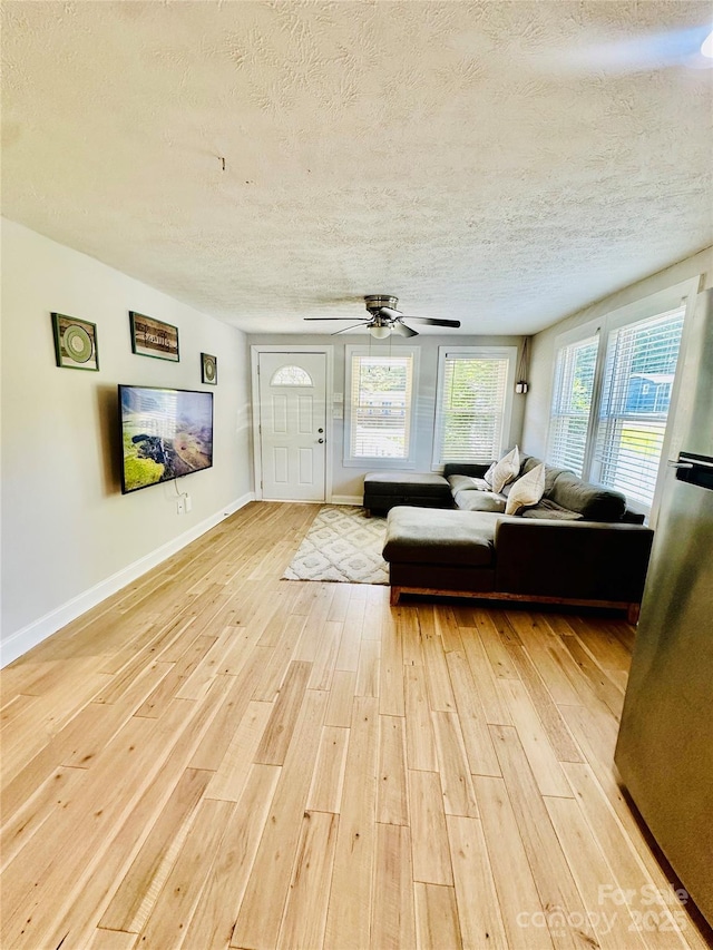 living area with a textured ceiling, light wood-style flooring, baseboards, and a ceiling fan