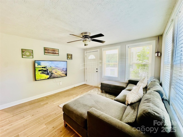 living area featuring baseboards, a textured ceiling, light wood-style floors, and a ceiling fan