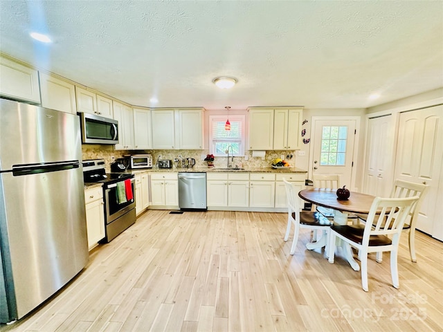 kitchen featuring appliances with stainless steel finishes, a sink, light wood-style floors, backsplash, and light stone counters
