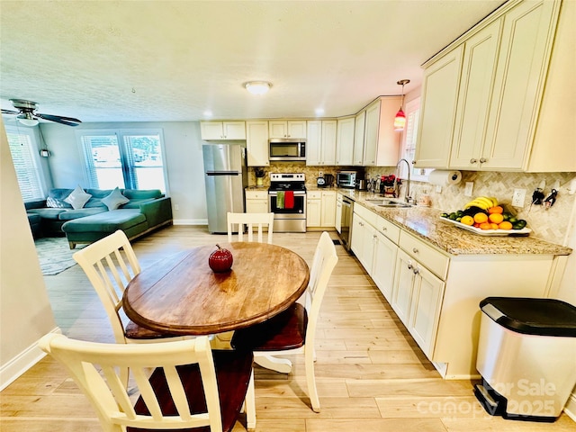 kitchen featuring stainless steel appliances, baseboards, backsplash, light wood-type flooring, and a sink