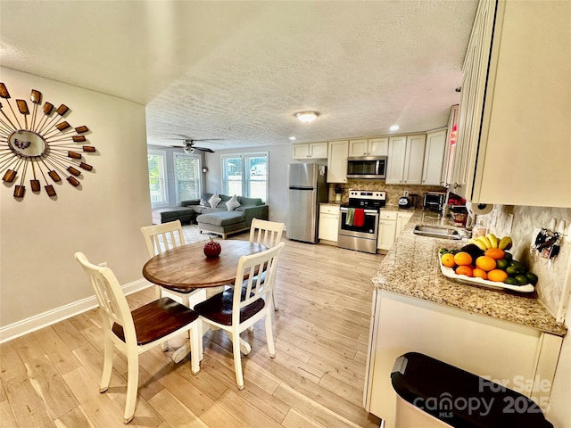dining space with a textured ceiling, light wood-style flooring, baseboards, and a ceiling fan