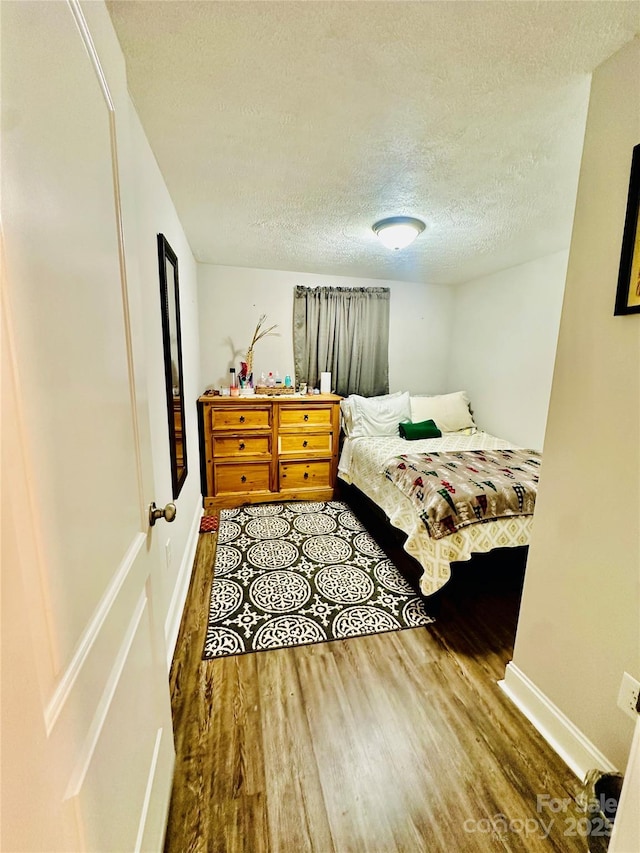 bedroom with wood finished floors, a textured ceiling, and baseboards