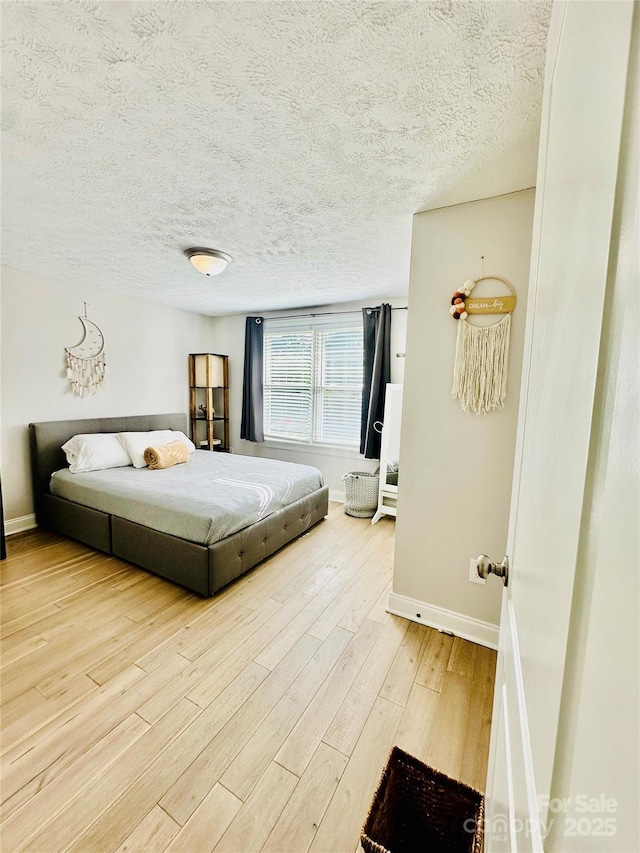 bedroom with baseboards, light wood-style flooring, and a textured ceiling