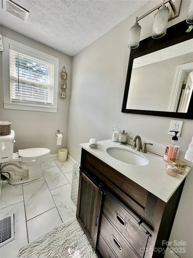 half bath featuring toilet, marble finish flooring, vanity, a textured ceiling, and baseboards