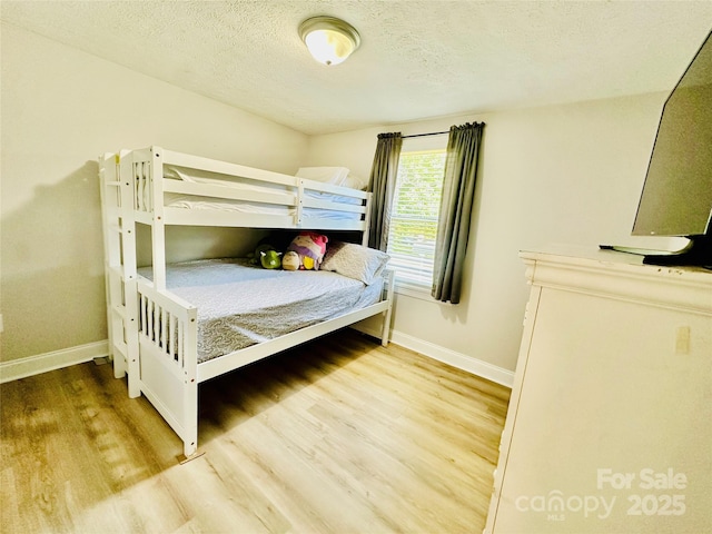 bedroom featuring baseboards, wood finished floors, and a textured ceiling
