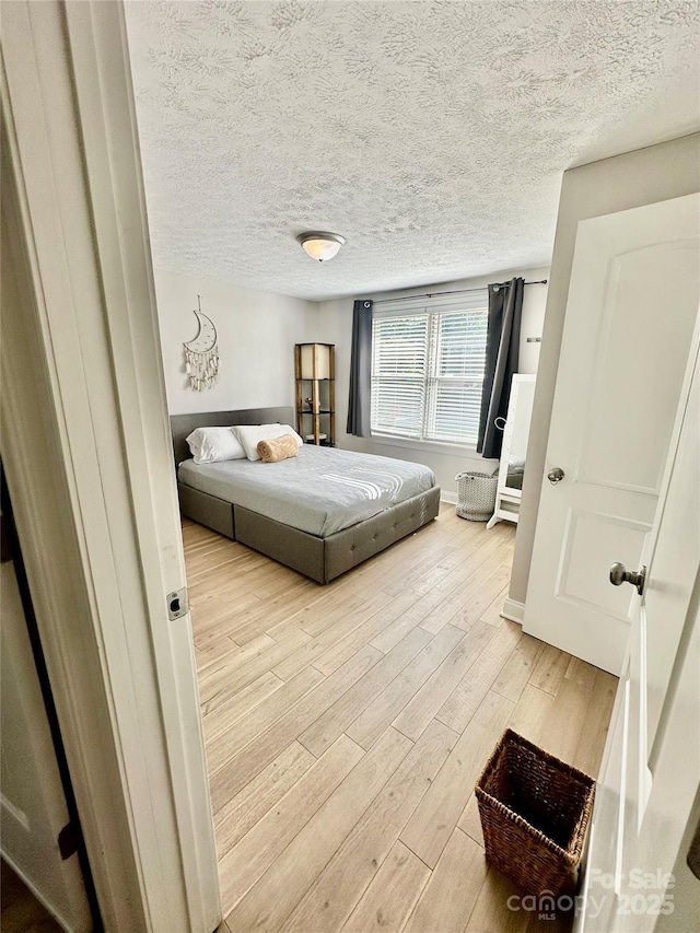bedroom featuring light wood finished floors, a textured ceiling, and baseboards