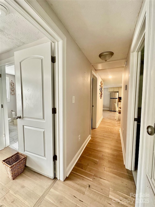 corridor featuring light wood-type flooring, baseboards, and a textured ceiling