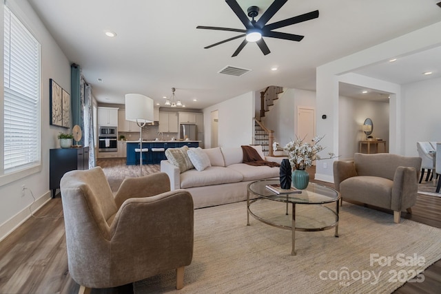 living area featuring recessed lighting, wood finished floors, stairs, ceiling fan with notable chandelier, and visible vents